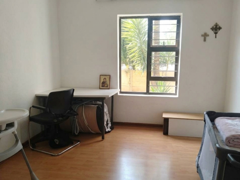 A functional bedroom featuring laminate flooring and a window fitted with security bars, providing natural light and a view of the exterior.