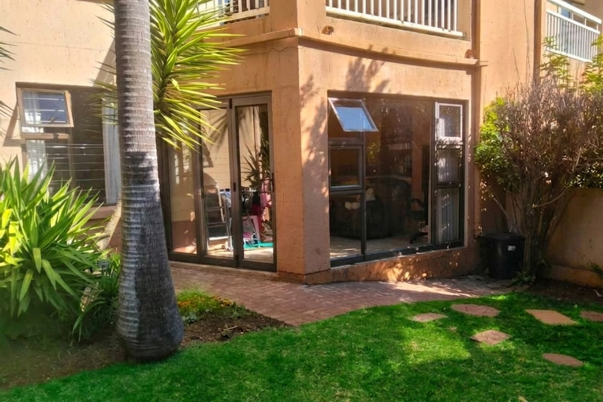 Rear view of the townhouse featuring a brick paved patio, aluminium sliding doors, and access to a private garden area.