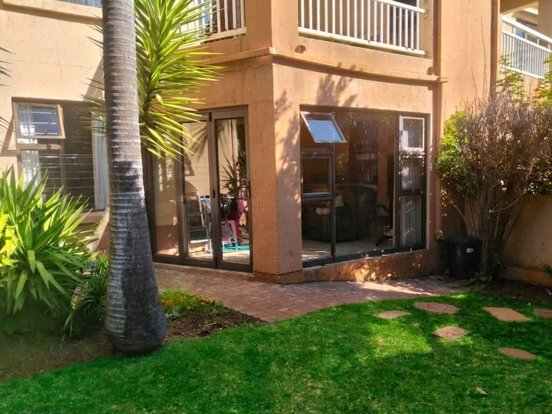 Rear view of the townhouse featuring a brick paved patio, aluminium sliding doors, and access to a private garden area.