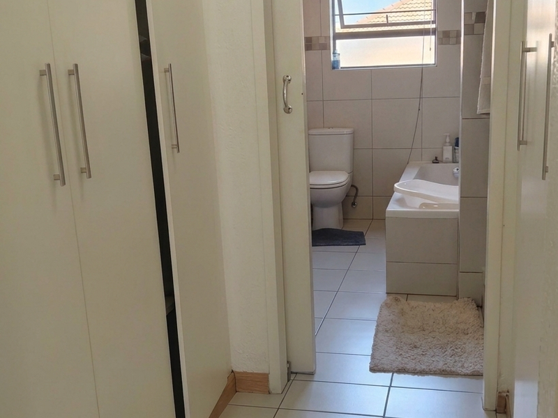 A functional bathroom featuring tiled walls and flooring, a bathtub, and a toilet, accessed via a sliding door from a hallway with built-in cupboards.