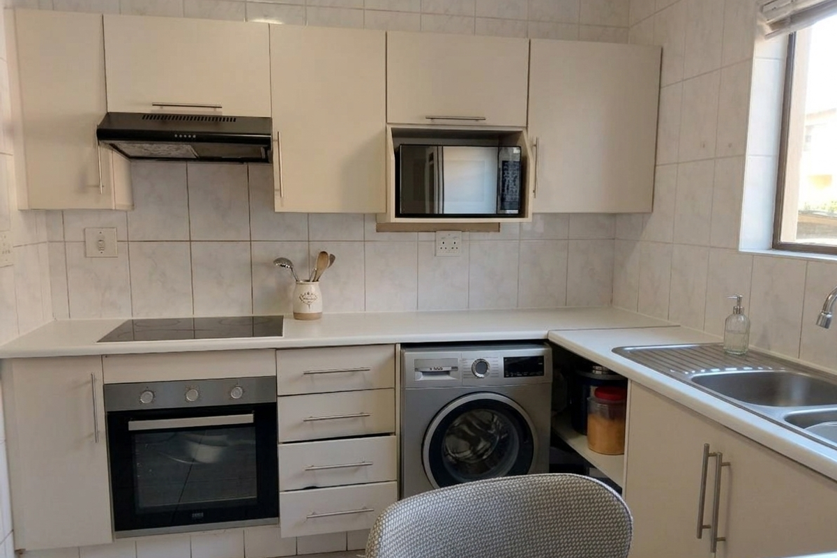 Functional kitchen featuring built-in cabinetry, electric hob, oven, extractor fan, and integrated laundry appliance space with a stainless steel sink.