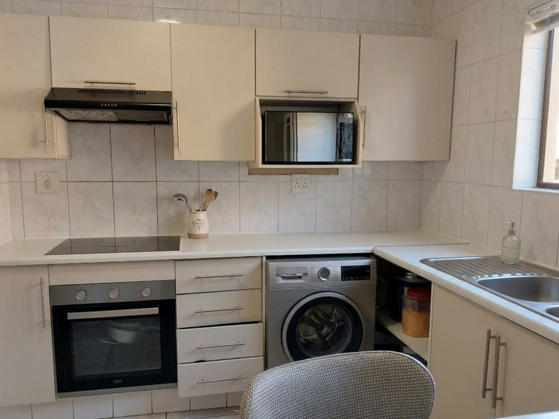 Functional kitchen featuring built-in cabinetry, electric hob, oven, extractor fan, and integrated laundry appliance space with a stainless steel sink.