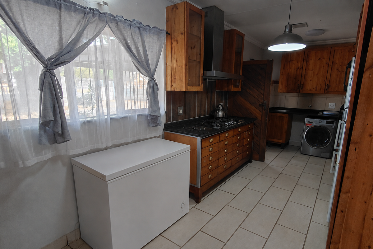 A functional kitchen featuring wooden cabinetry, a gas hob with extractor fan, and tiled flooring, offering a practical layout for daily meal preparation.
