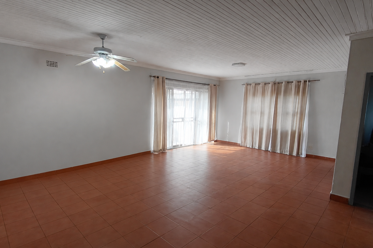 A spacious, empty living room featuring tiled flooring, a ceiling fan, and a timber-look ceiling, offering a blank canvas for interior design.