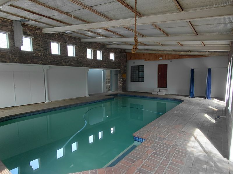 Spacious indoor swimming pool area featuring exposed brick walls, a high exposed beam ceiling, and tiled surrounds, offering a versatile recreational space.