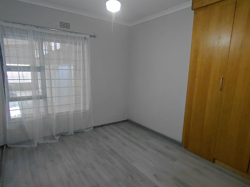 A clean, empty bedroom featuring light-toned laminate flooring, a built-in wooden wardrobe, and a ceiling fan.