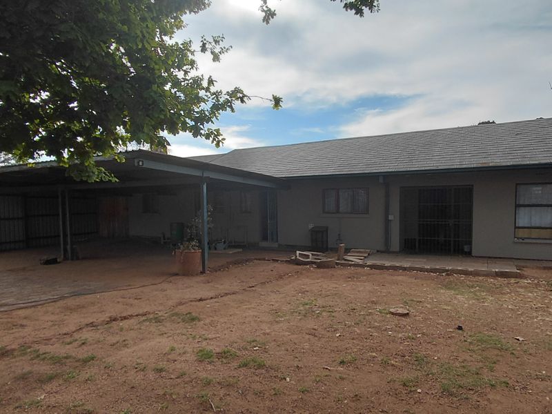 Rear view of the property featuring a large carport, paved patio area, and an expansive, unlandscaped backyard.