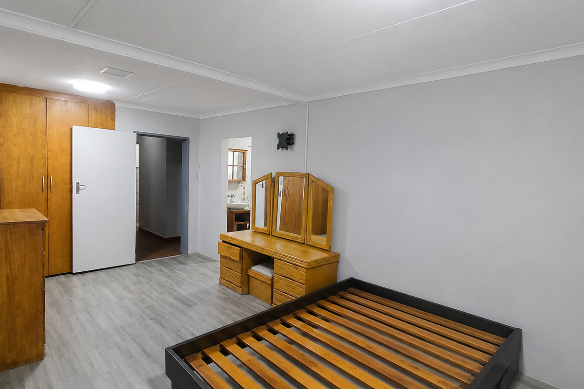 A spacious bedroom featuring built-in wooden cupboards, laminate flooring, and neutral wall finishes, with direct access to an adjoining room.
