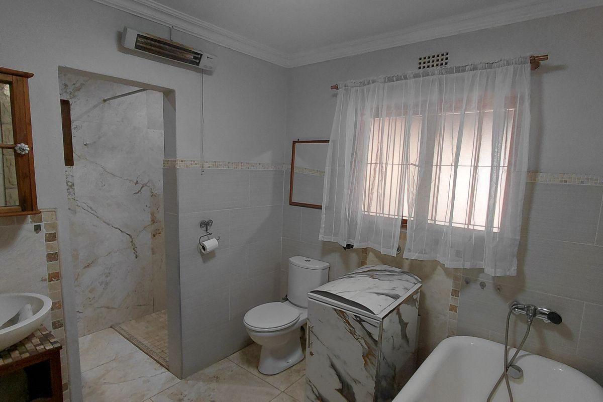 A functional bathroom featuring a walk-in shower, bathtub, vessel sink, and wall-mounted heater with neutral tiled finishes throughout.