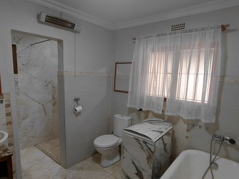 A functional bathroom featuring a walk-in shower, bathtub, vessel sink, and wall-mounted heater with neutral tiled finishes throughout.