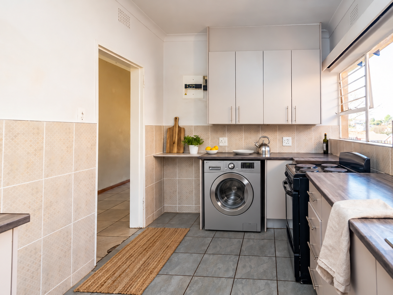 A functional kitchen featuring built-in cabinetry, laminate countertops, a tiled splashback, and a freestanding stove, with tiled flooring throughout.
