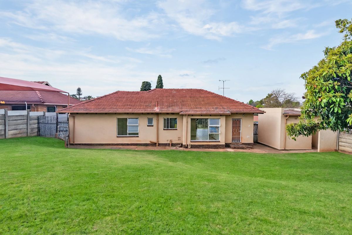 Rear view of a single-story house featuring a tiled roof, concrete perimeter wall, and a spacious backyard lawn.