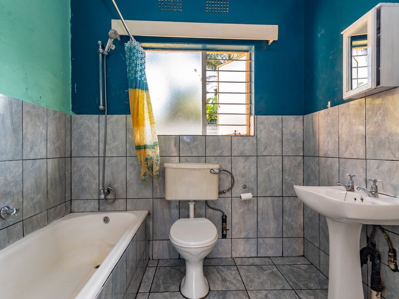 A functional bathroom featuring a bathtub, pedestal sink, and toilet with tiled finishes, offering potential for modernization and cosmetic updates.