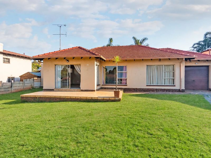 Rear view of a single-story house featuring a tiled roof, a paved patio area, and a spacious lawn with a garage.