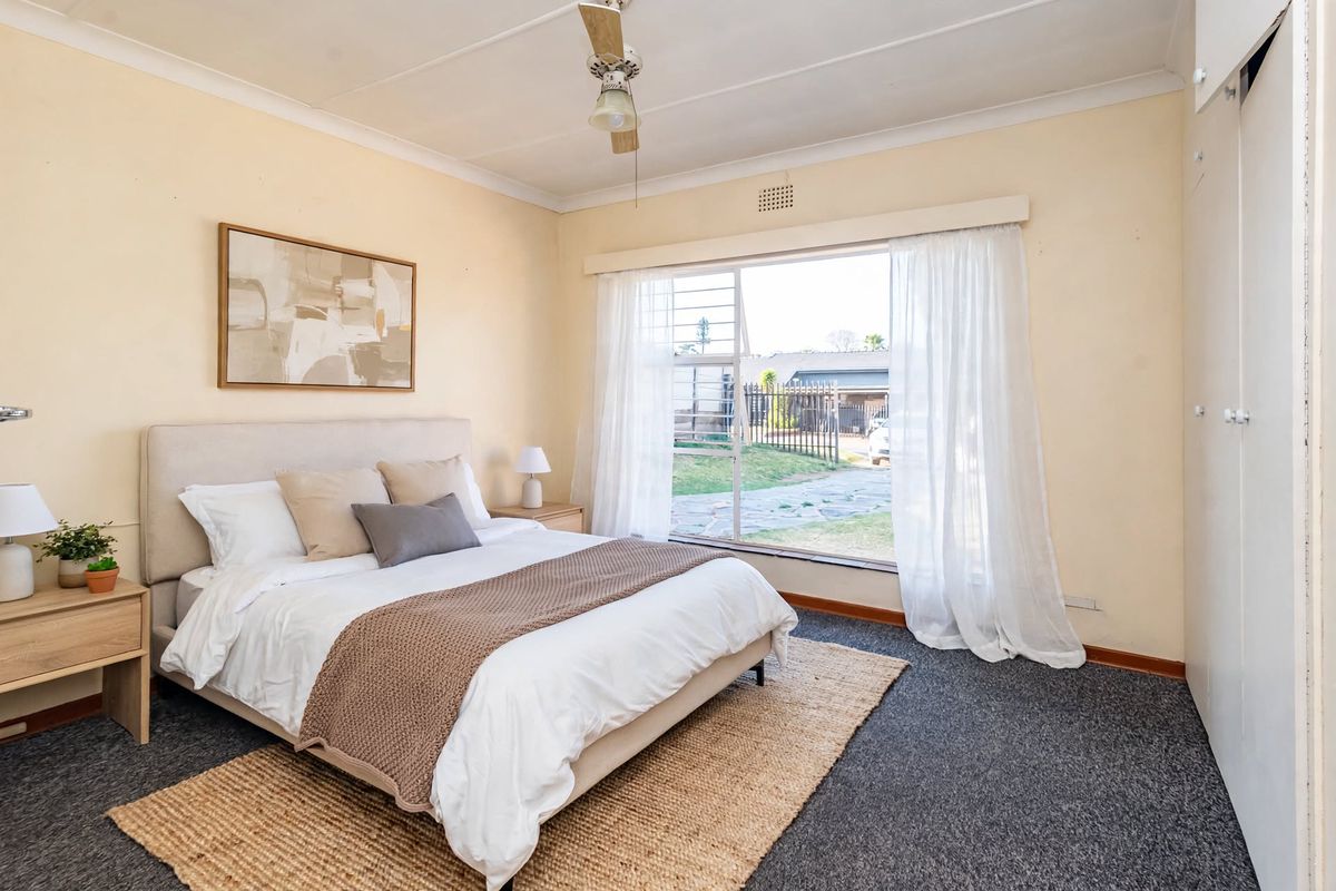 A well-lit bedroom featuring built-in cupboards, carpeted flooring, and a large window providing natural light and views of the front garden.
