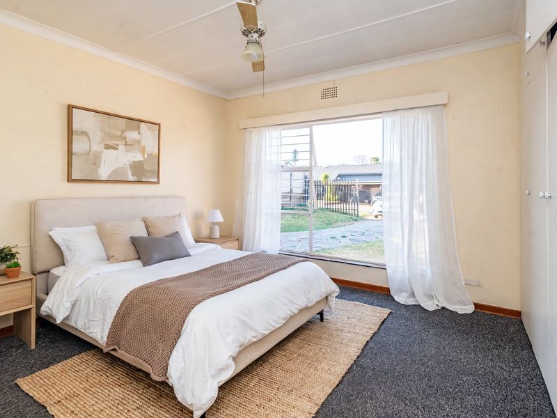 A well-lit bedroom featuring built-in cupboards, carpeted flooring, and a large window providing natural light and views of the front garden.
