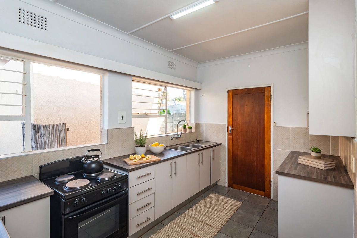 A functional kitchen featuring white cabinetry, dark laminate countertops, a double bowl sink, and a freestanding electric stove with a tiled backsplash.