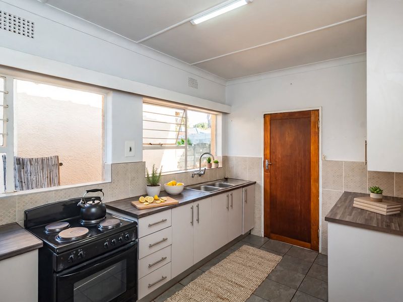 A functional kitchen featuring white cabinetry, dark laminate countertops, a double bowl sink, and a freestanding electric stove with a tiled backsplash.
