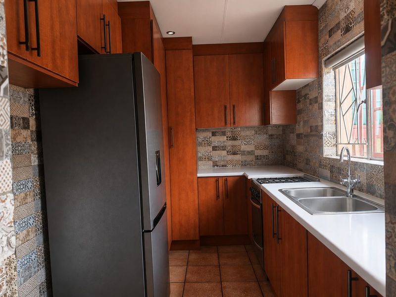 A well-maintained kitchen featuring warm-toned wooden cabinetry, a tiled backsplash, white countertops, a double sink, and a built-in gas hob and oven.