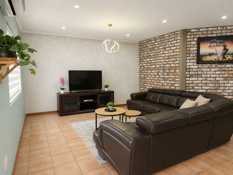 A well-maintained living room featuring a distinctive exposed brick feature wall, neutral tiled flooring, and modern recessed lighting.