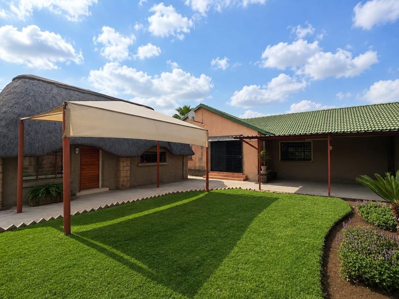 A well-maintained rear courtyard featuring a manicured lawn, paved patio area, and a combination of thatch and tiled roof structures.