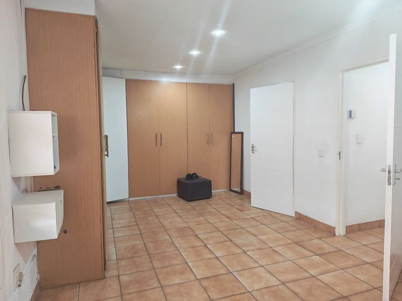 A spacious bedroom featuring neutral tiled flooring, ample built-in cupboard storage, and recessed ceiling lighting.