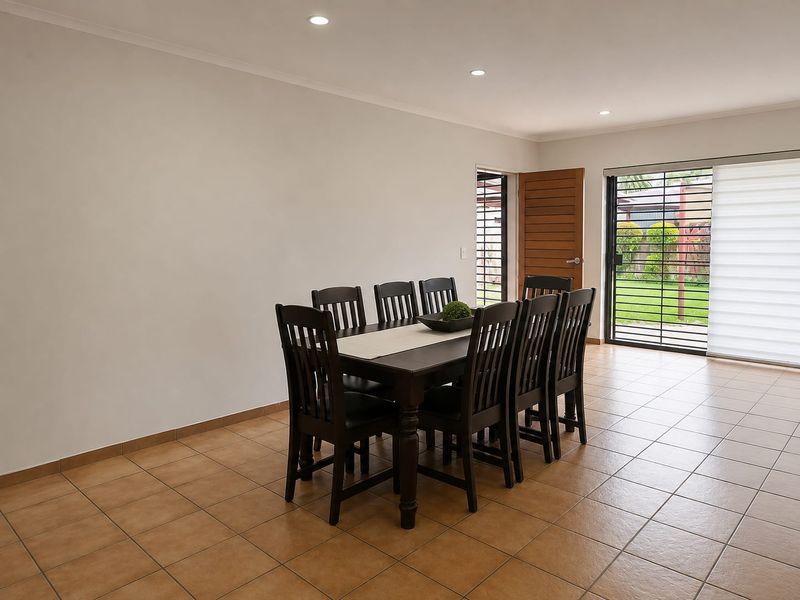 A bright dining room featuring neutral walls, ceramic tiled flooring, recessed lighting, and direct access to the garden through a sliding glass door.