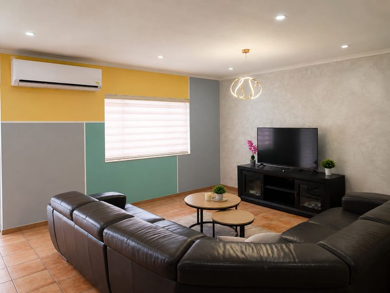 A well-maintained living room featuring tiled flooring, recessed downlighting, and a wall-mounted split-system air conditioner.