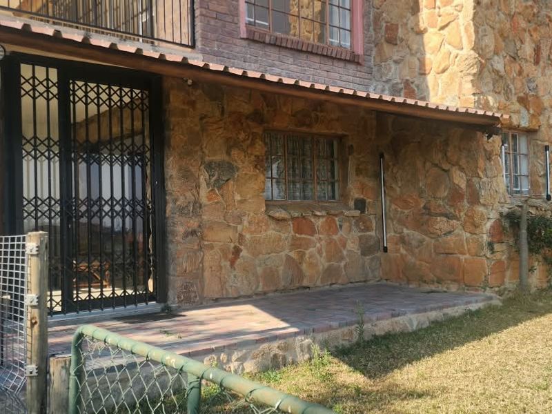 A covered patio area featuring rustic stone cladding, brick accents, and a secure metal gate, overlooking the surrounding farm garden.