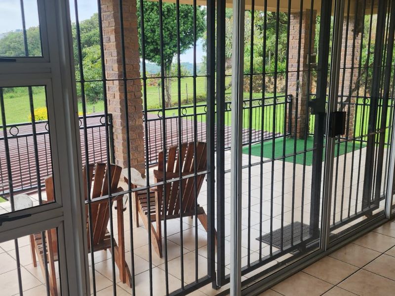 A covered patio area featuring brick pillars, tiled flooring, and metal security gates, offering a view of the surrounding farm landscape.
