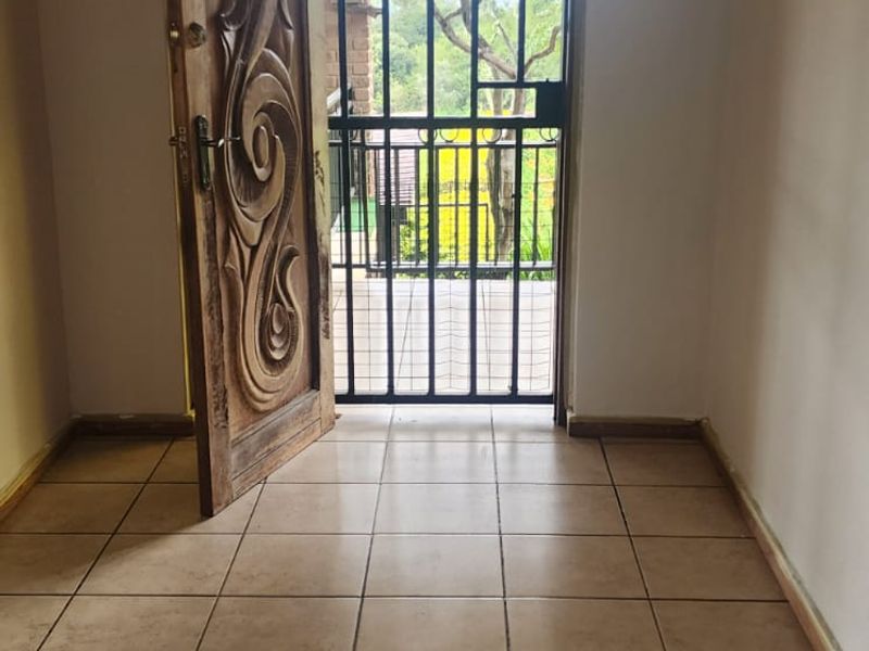 An empty entrance area featuring tiled flooring, a decorative carved wooden door, and a metal security gate leading to the exterior.