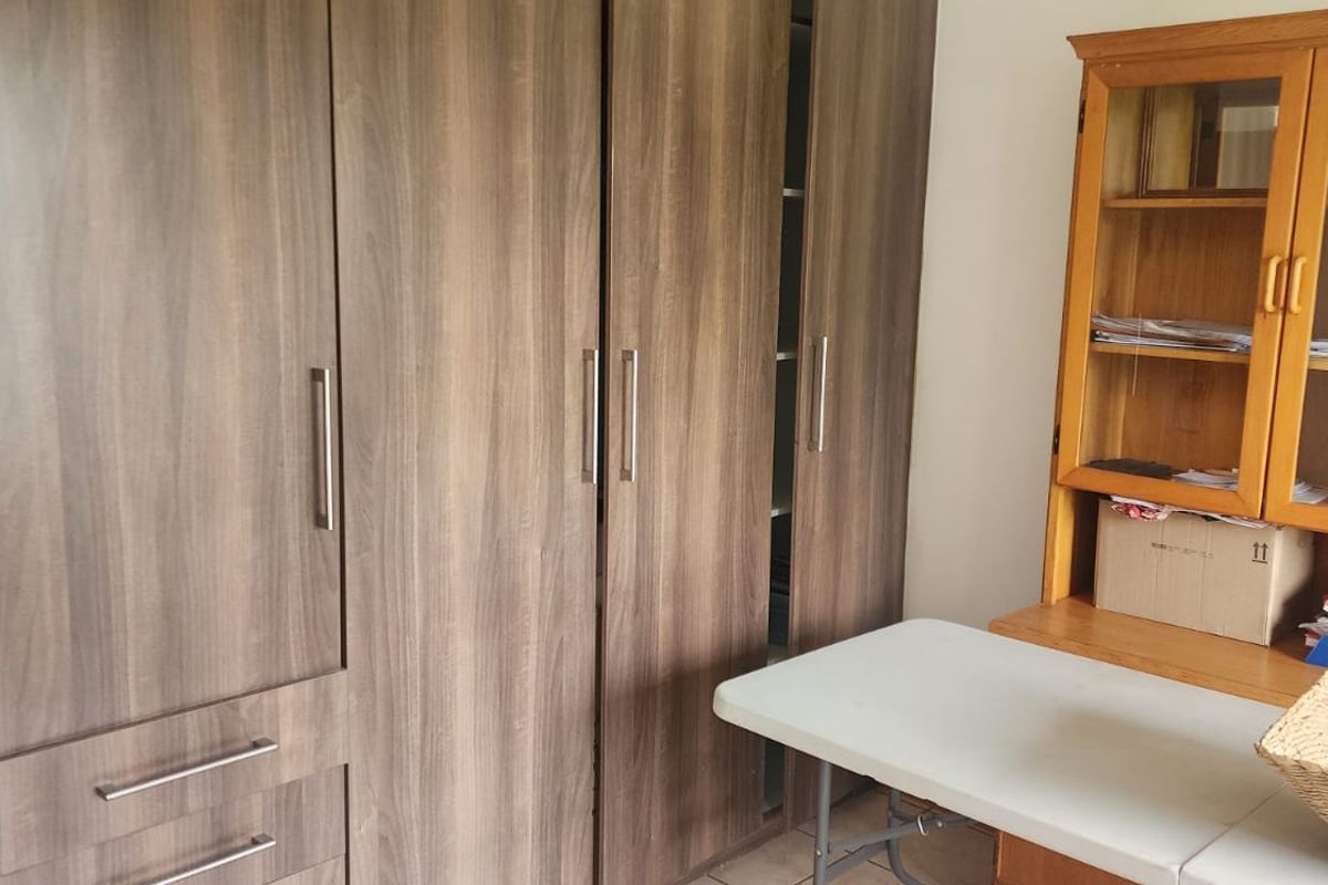A bedroom featuring floor-to-ceiling built-in wooden cupboards with modern metal handles, providing ample storage space.