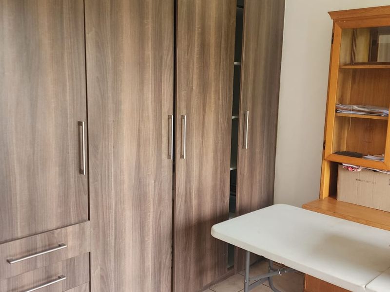 A bedroom featuring floor-to-ceiling built-in wooden cupboards with modern metal handles, providing ample storage space.