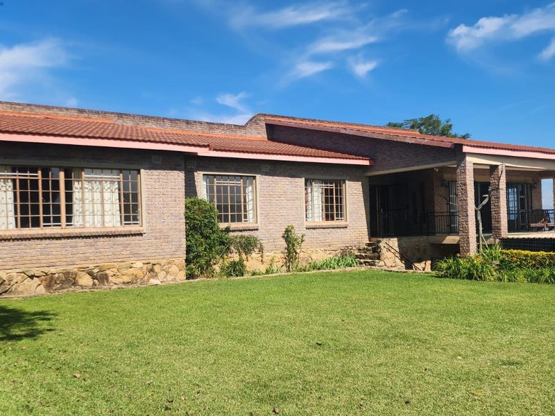 A well-maintained brick farmhouse featuring a tiled roof, stone foundation, and a spacious covered patio overlooking a large green lawn.