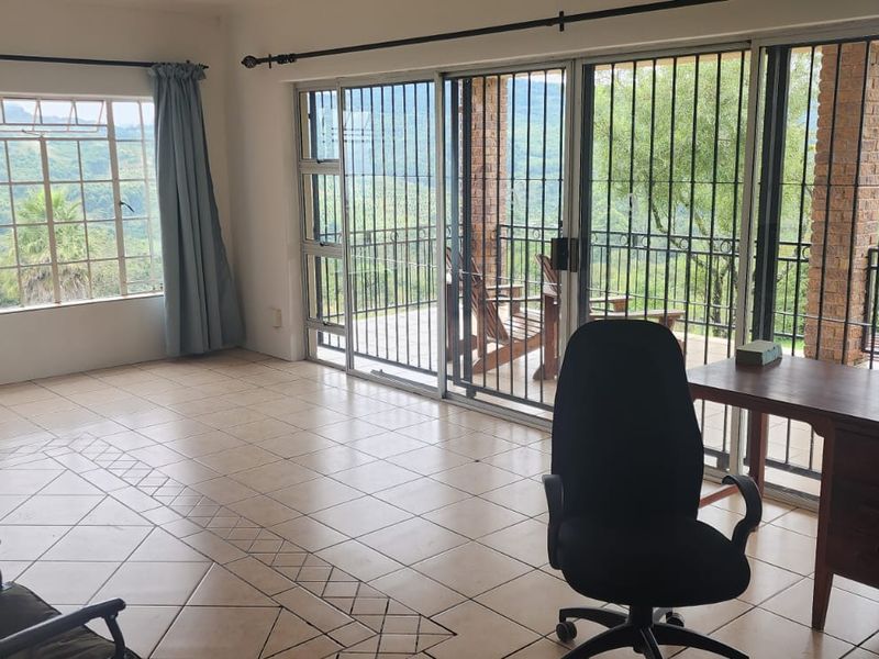 Spacious living area featuring ceramic tile flooring, large windows, and sliding glass doors that open to a scenic outdoor patio with security bars.