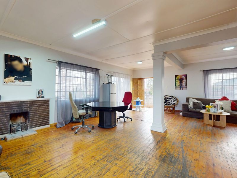 Spacious living area featuring original hardwood flooring, a brick fireplace, and an open-plan layout with a central support column.