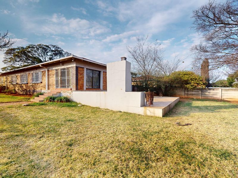 Rear view of the property featuring a brick facade, security bars on windows, and a concrete patio area with a built-in outdoor fireplace.