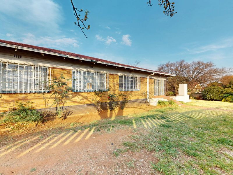 Rear view of a single-story brick house featuring a tiled roof, security bars on windows, and an expansive garden area.
