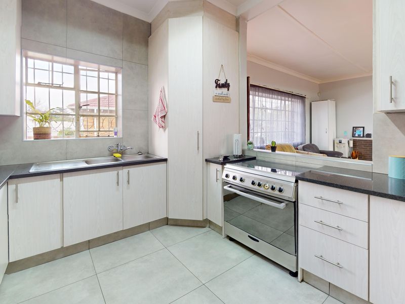A functional kitchen featuring light wood-grain cabinetry, granite countertops, a stainless steel stove, and a double basin sink with a tiled backsplash.
