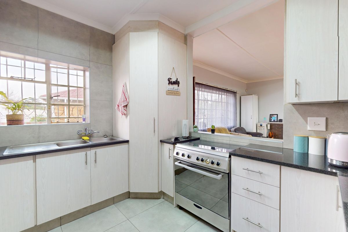 A functional kitchen featuring light-toned cabinetry, granite countertops, a stainless steel sink, and a freestanding stove, with an open-plan view into the living area.