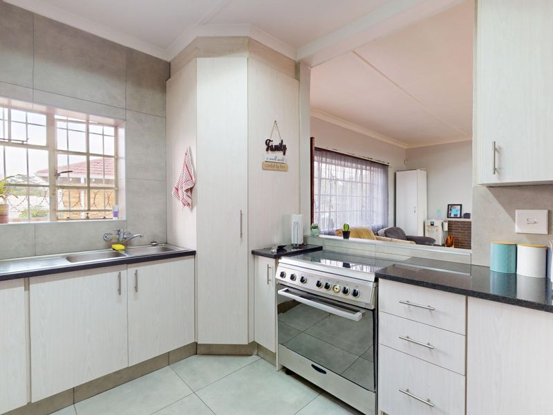 A functional kitchen featuring light-toned cabinetry, granite countertops, a stainless steel sink, and a freestanding stove, with an open-plan view into the living area.