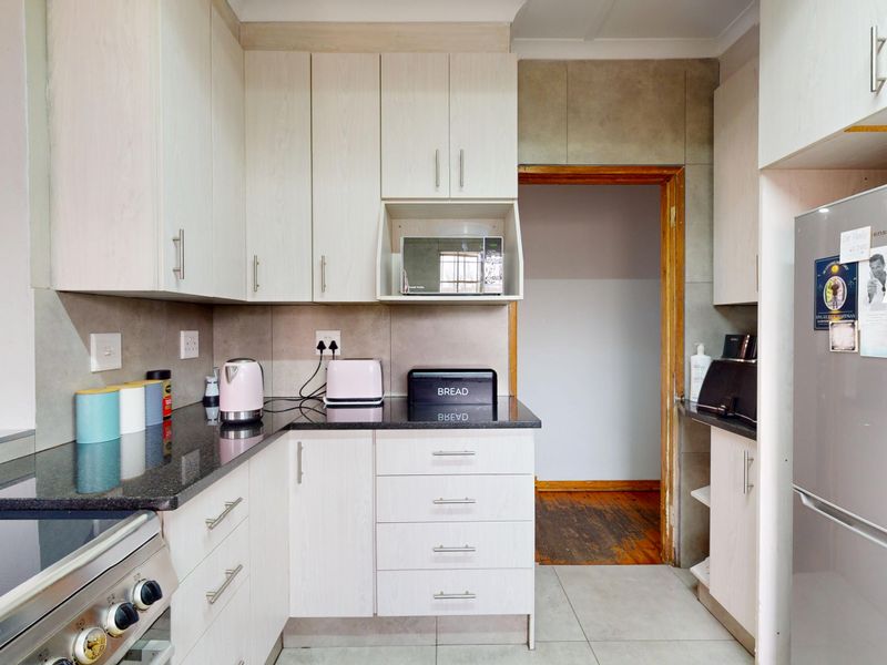 A functional kitchen featuring light-toned cabinetry, dark granite countertops, a built-in microwave, and tiled flooring with a doorway leading to an adjacent room.