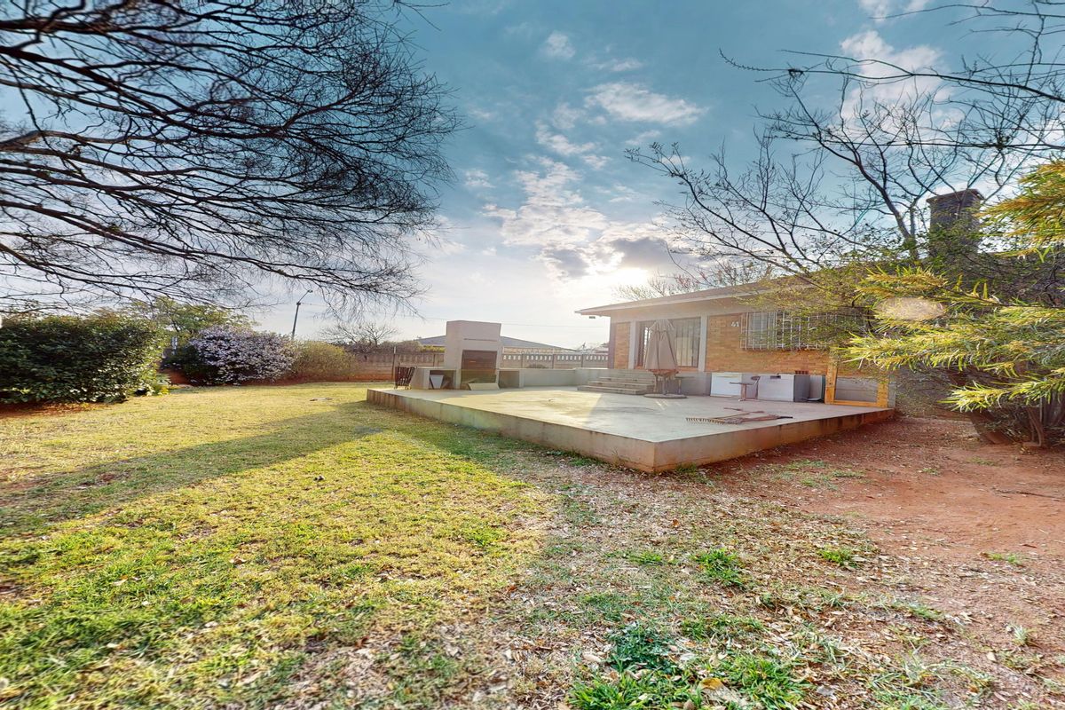 Rear view of the property featuring a concrete patio area with a built-in braai and a spacious garden.