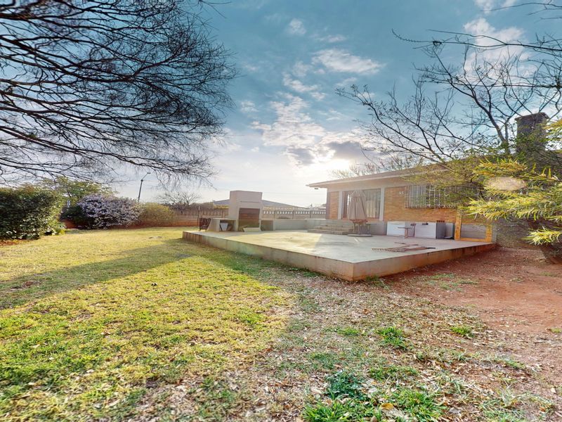 Rear view of the property featuring a concrete patio area with a built-in braai and a spacious garden.