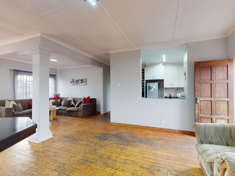 Open-plan living area featuring hardwood flooring, a structural column, and a pass-through window connecting to the kitchen.