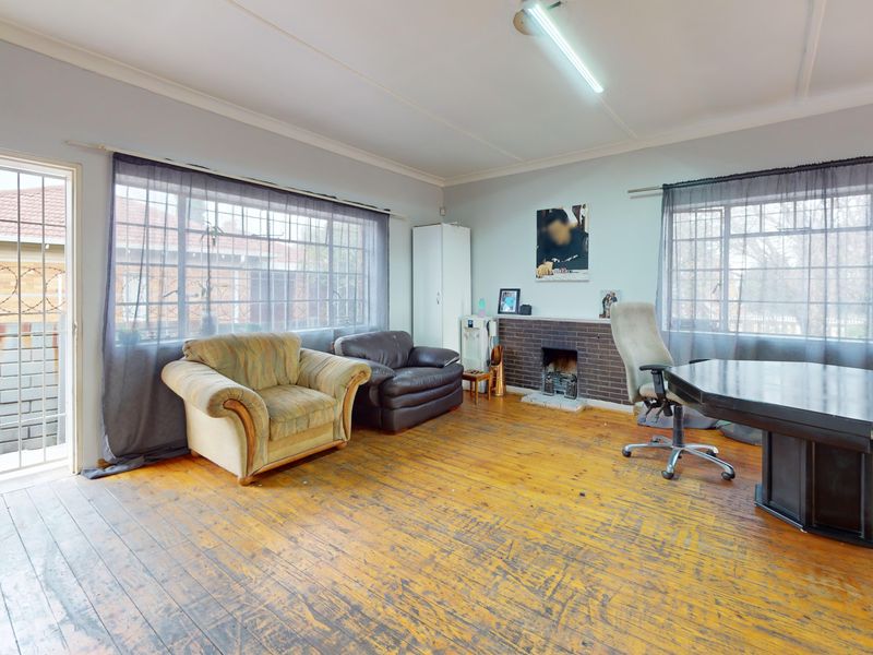 Spacious living room featuring original timber flooring, a brick fireplace, and large windows with security bars, offering potential for modernization and cosmetic updates.