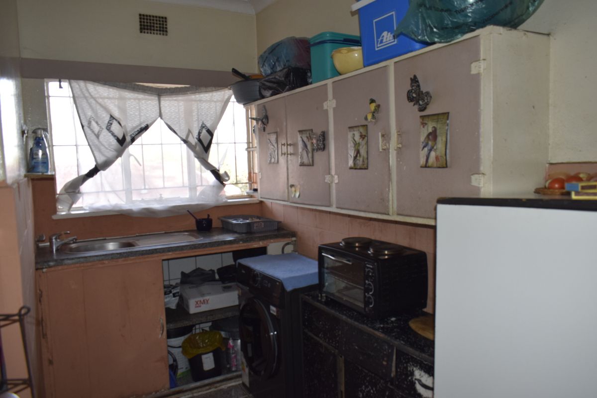 A compact kitchen featuring original built-in cabinetry, a stainless steel sink, and security bars on the window, offering potential for modernization.