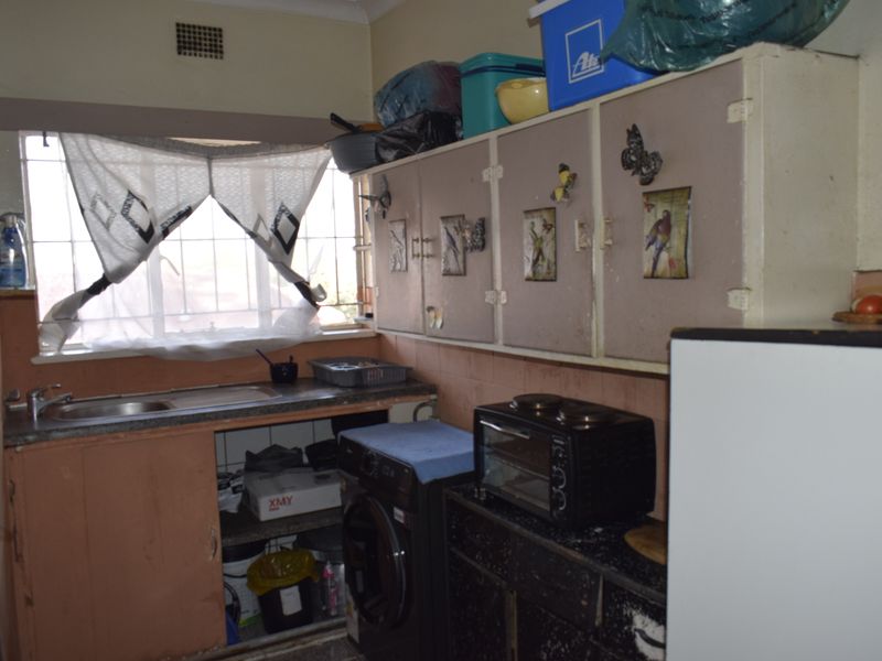 A compact kitchen featuring original built-in cabinetry, a stainless steel sink, and security bars on the window, offering potential for modernization.