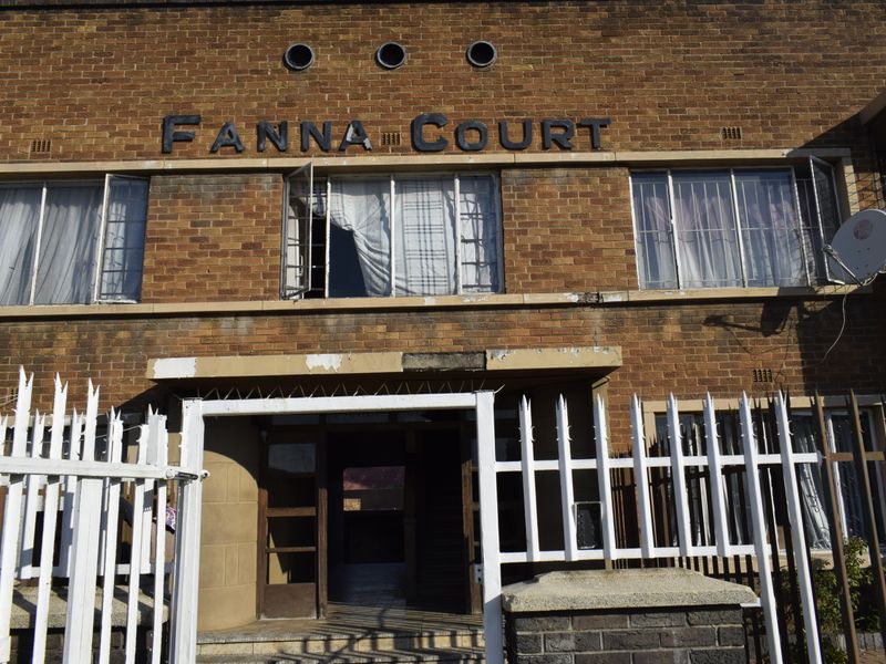 Front elevation of Fanna Court apartment building featuring brick facade, security gate, and steel-framed windows with security bars.