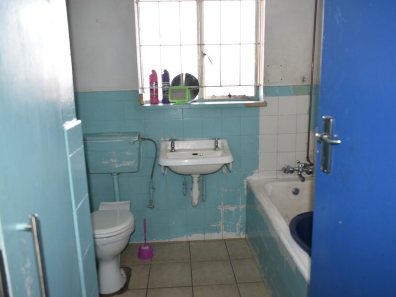 A dated bathroom featuring original wall tiles, a wall-mounted basin, a bathtub, and a toilet, requiring significant renovation and modernization.